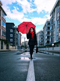 Full length of young woman with red umbrella walking on wet street