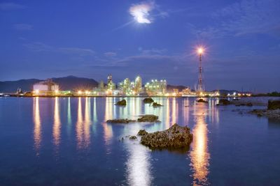 Illuminated buildings by sea against sky at night