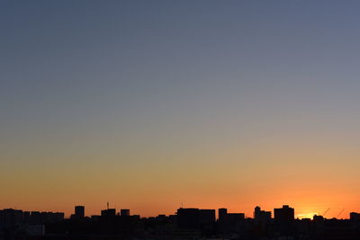 Silhouette cityscape against clear sky during sunset