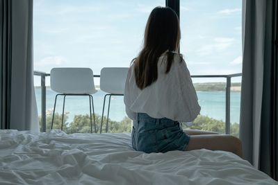 Rear view of woman sitting on bed at home