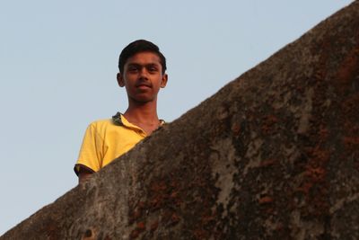 Portrait of boy on rock against clear sky