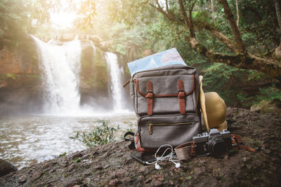 Backpack, map, hat, smart phone, earphone and camera at front of the waterfall.