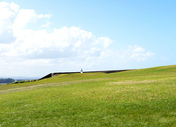 Scenic view of grassy hill against cloudy sky on sunny day