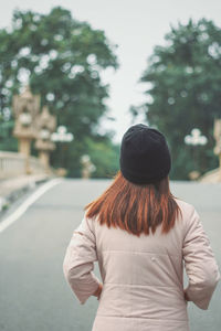 Rear view of woman standing against trees in city