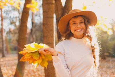 Portrait of young woman wearing hat standing against tree