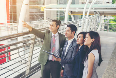 Smiling businessman showing something to colleagues standing on elevated walkway 