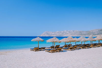 Deck chairs on beach against clear blue sky