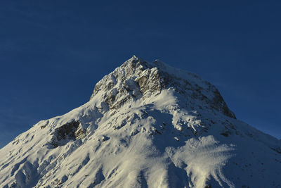 Low angle view of snowcapped mountain against blue sky