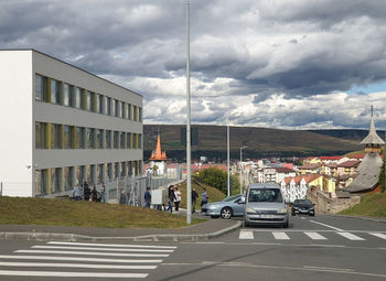 Cars on road by buildings against sky in city