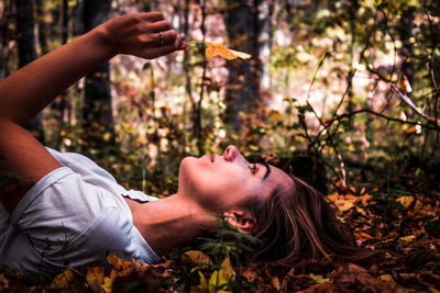 Young woman holding maple leaf while lying in forest