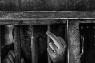 Portrait of man gesturing while standing prison bars