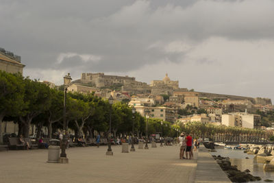 People walking in city against cloudy sky