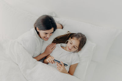 High angle view of mother and daughter looking at smart phone lying on bed