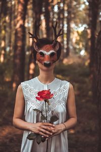 Close-up of woman holding rose while wearing mask in forest