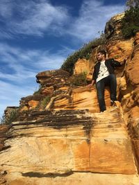 Low angle view of young man standing on rock against blue sky during sunny day