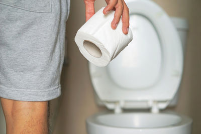 Midsection of man holding toilet paper while standing in bathroom