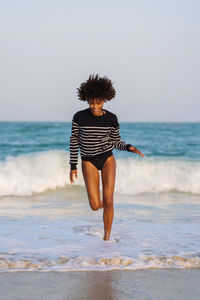 Woman with afro hair having fun at the beach running from the waves