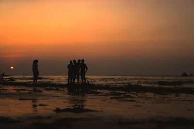 Silhouette people standing on beach against sky during sunset