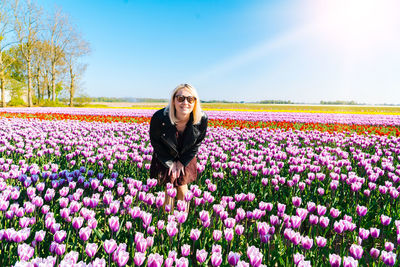 Young woman standing on field by flowering plants against sky