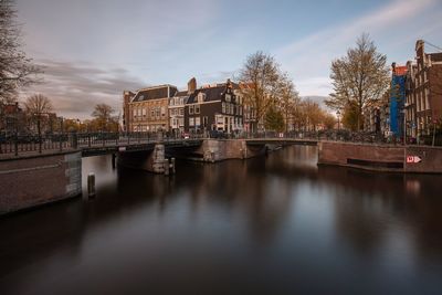 Bridge over river by buildings against sky in city