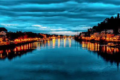 River by illuminated city against sky at dusk