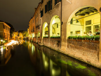 Illuminated buildings by lake against sky in city at night