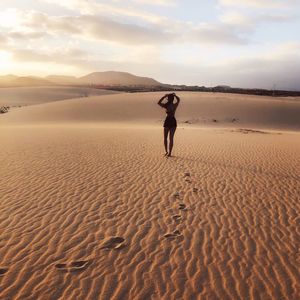 Rear view of man on sand dune in desert against sky