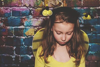 Sad girl wearing bumblebee costume standing against wall