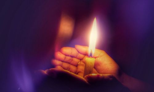 Cropped image of hands covering lit candle