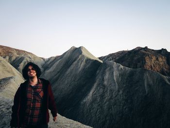 Portrait of smiling young man standing on mountain against clear sky