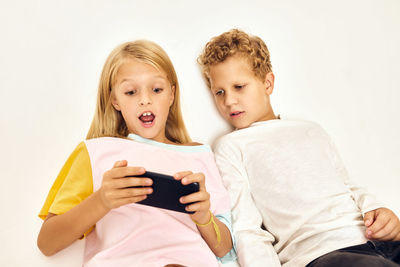 Portrait of smiling girl using digital tablet while sitting against wall