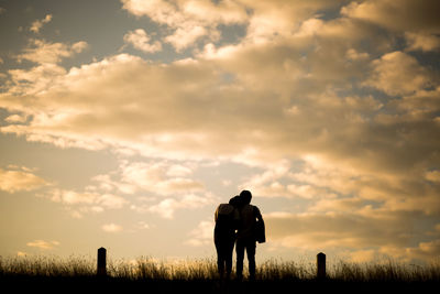 Rear view of men standing on field against sky during sunset