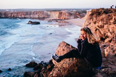 Young woman sitting on cliff against sea