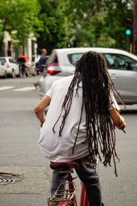 Rear view of man with dreadlocks riding bicycle in city