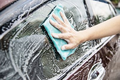 Cropped hands of man cleaning car windows