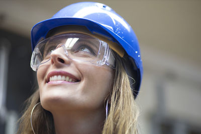 Close-up of smiling woman wearing hardhat looking up