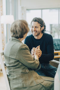 Smiling man holding hands while talking to grandmother at elderly nursing home