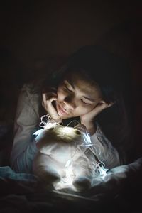 Young woman looking at stuffed toy with illuminated string lights on bed at home