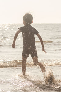 Side view of shirtless boy running in sea