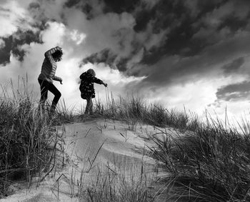 Low angle view of girls walking on hill against cloudy sky