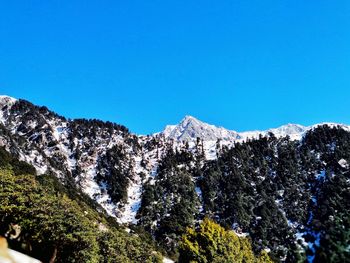 Low angle view of snowcapped mountains against clear blue sky