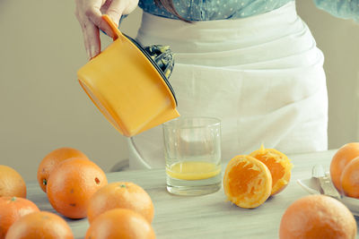 Midsection of woman pouring juice of orange on table