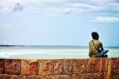 Rear view of man sitting at beach against sky