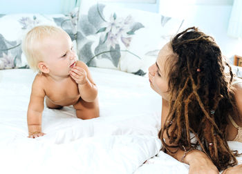 Mother playing with naked daughter on bed at home