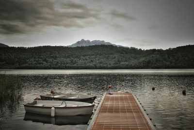 Pier on calm lake against cloudy sky