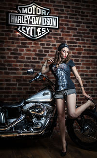 Portrait of young woman standing by motorcycle against brick wall
