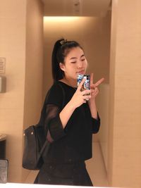 Young woman using phone while standing on mirror