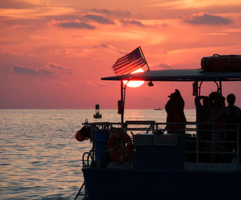 People on boat at sea photographing scenic sunset
