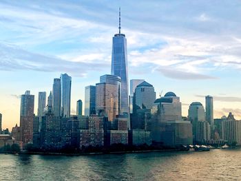 View of buildings in city at waterfront against cloudy sky