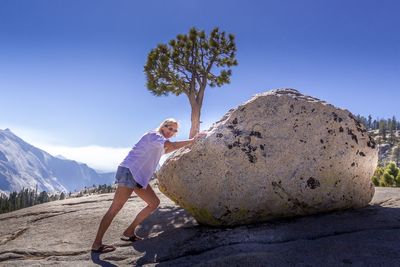 Mature woman leaning on rock formation against blue sky
